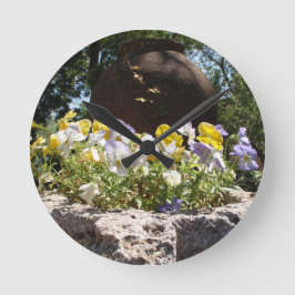 Reloj Redondo Mediano Violetas en un abrevadero de piedra.