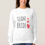 Sudadera Novia de equipo<br><div class="desc">Impresionante diseño con la cita "Novia en equipo" y tres corazones rojos. Una idea estupenda y divertida para una soltera o para la fiesta de bodas.</div>