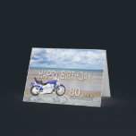 Tarjeta 80th birthday card with a motor bike<br><div class="desc">A blue motor cycle standing on a beach with fluffy clouds in the sky. Happy Birthday written in rock reflected in the water lying on the sand.</div>