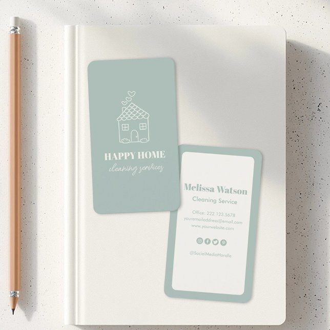 Tarjeta De Visita Moderno Servicio De Limpieza Elegante De Casa (Two business cards on a white notebook. One card has a house sketch with Happy Home Cleaning Service)
