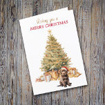 Tarjeta Festiva Cachorro de cachorro de chocolate de árbol de oro<br><div class="desc">En la parte delantera de esta tarjeta de Navidades, un adorable cachorro Labrador Retriever de chocolate lleva un sombrero de Santa Claus rojo y blanco y se sienta frente a un árbol de vacaciones. El árbol está decorado en oro, y debajo hay paquetes de regalos a juego. El texto dorado...</div>