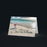 Tarjeta Festiva Navidades tropicales Snowman en una playa<br><div class="desc">Un pequeño muñeco de nieve de arena con un sombrero de Santa se para en una playa de arena con "Feliz Navidad" escrito en la arena</div>