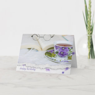 Tarjeta taza vintage de té de pansy sobre piel con libro