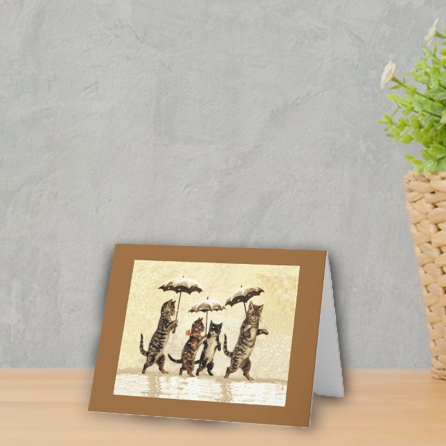 Tarjetas de gatos en la nieve con paraguas (Four cats walking upright in snow with umbrellas on yellow with brown frame notecard.)