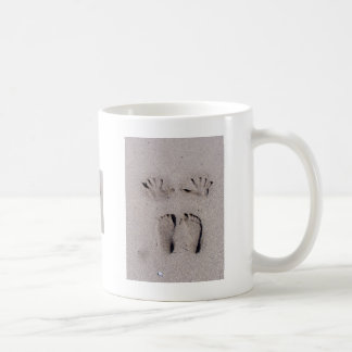 Taza De Café La mano y los pies imprime en arena de la playa de
