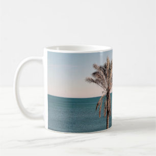 Taza De Café Palmera en la orilla de la playa por la mañana