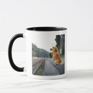 Taza Perro que se sienta en la estación de tren