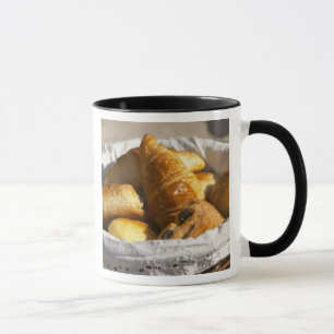 Taza Una cesta de desayuno de mimbre con cruasanes, y
