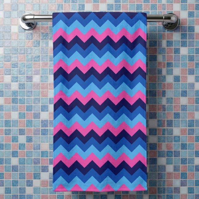 Toalla de baño con patrón de chevron azul rosa (Cool Blue Pink Chevron Pattern Bath Towel hanging on a rack in a bathroom against tiled wall.)