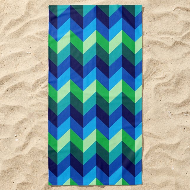 Toalla de playa con chevrones ombré azul verde (Blue Green Ombre Chevrons Beach Towel lying in the sand.)