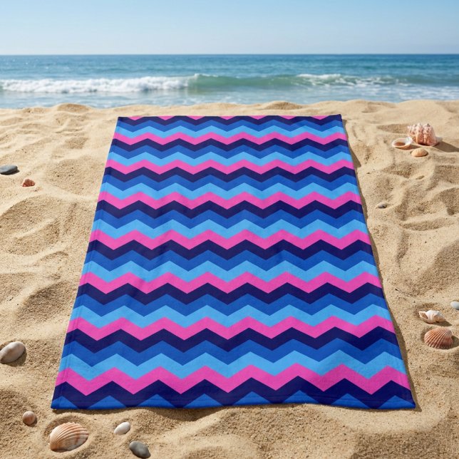 Toalla de playa con patrón de chevron azul rosa Co (Cool Blue Pink Chevron Pattern Beach Towel laying on sandy beach near an ocean.)