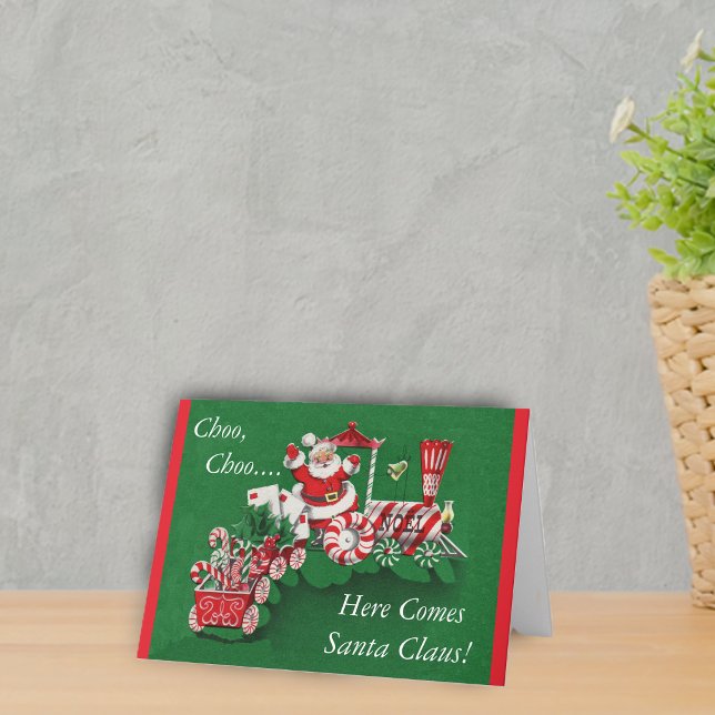 Tren de Navidad de Santa (Santa riding peppermint candy train with letters on a greem Merry Christmas Here comes Santa Card.)